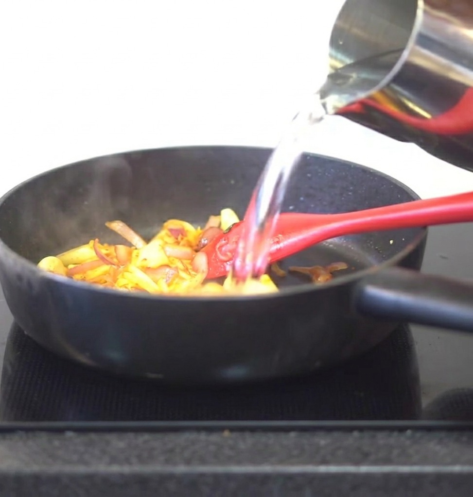 Woda wlewana z metalowego dzbanka na patelnię z podsmażonym kimchi i aromatami.