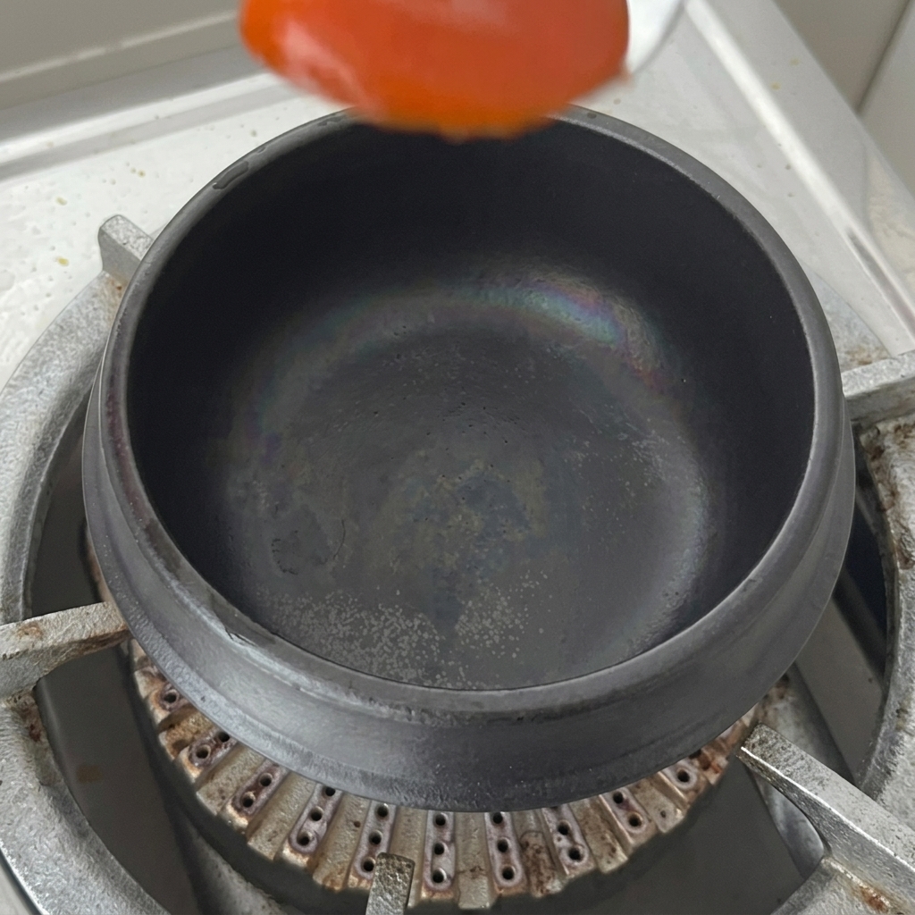 Łyżka ostrego sosu chili umieszczana na dnie suchego czarnego glinianego garnka na kuchence.