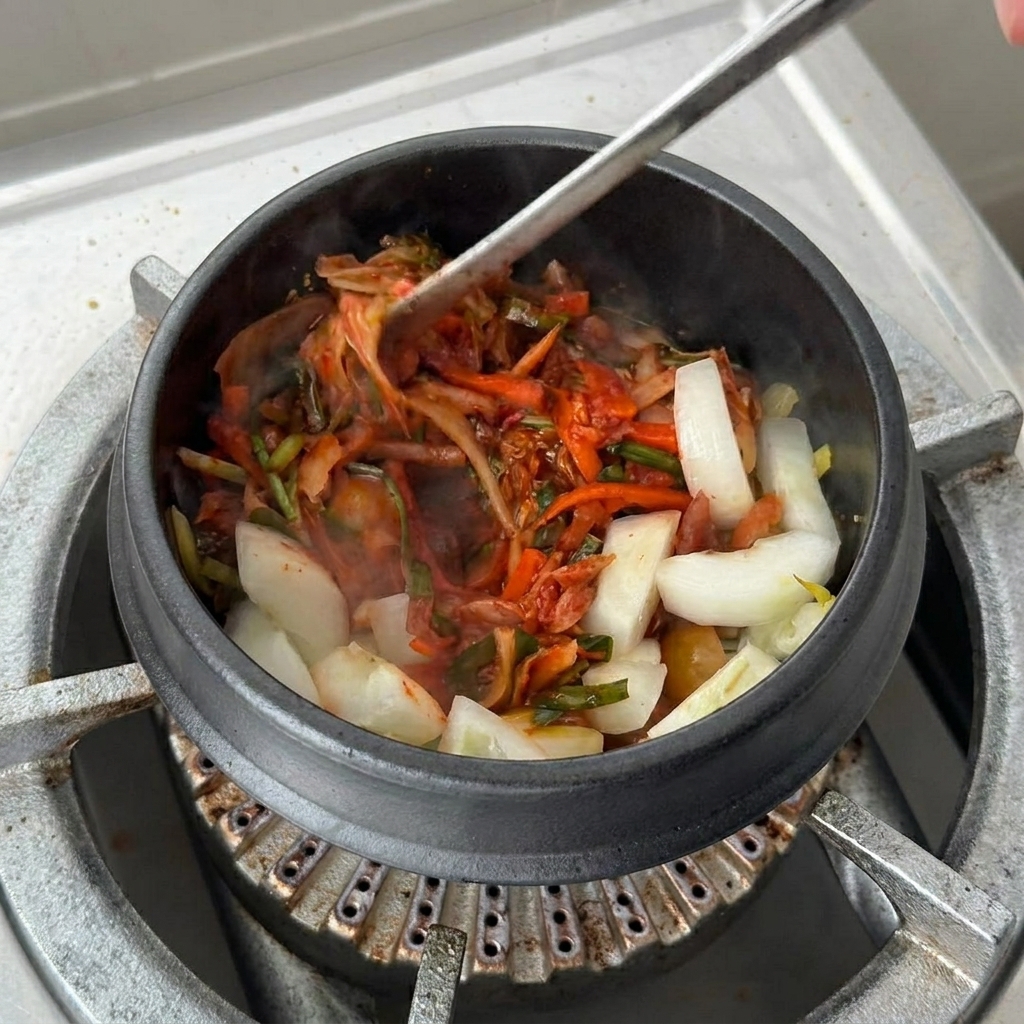 Szklanka soku z kimchi wlewana do garnka na podsmażone składniki.