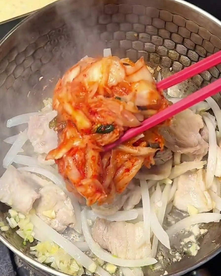 Czerwone, przyprawione kimchi mieszane z boczkiem i cebulą w garnku.
