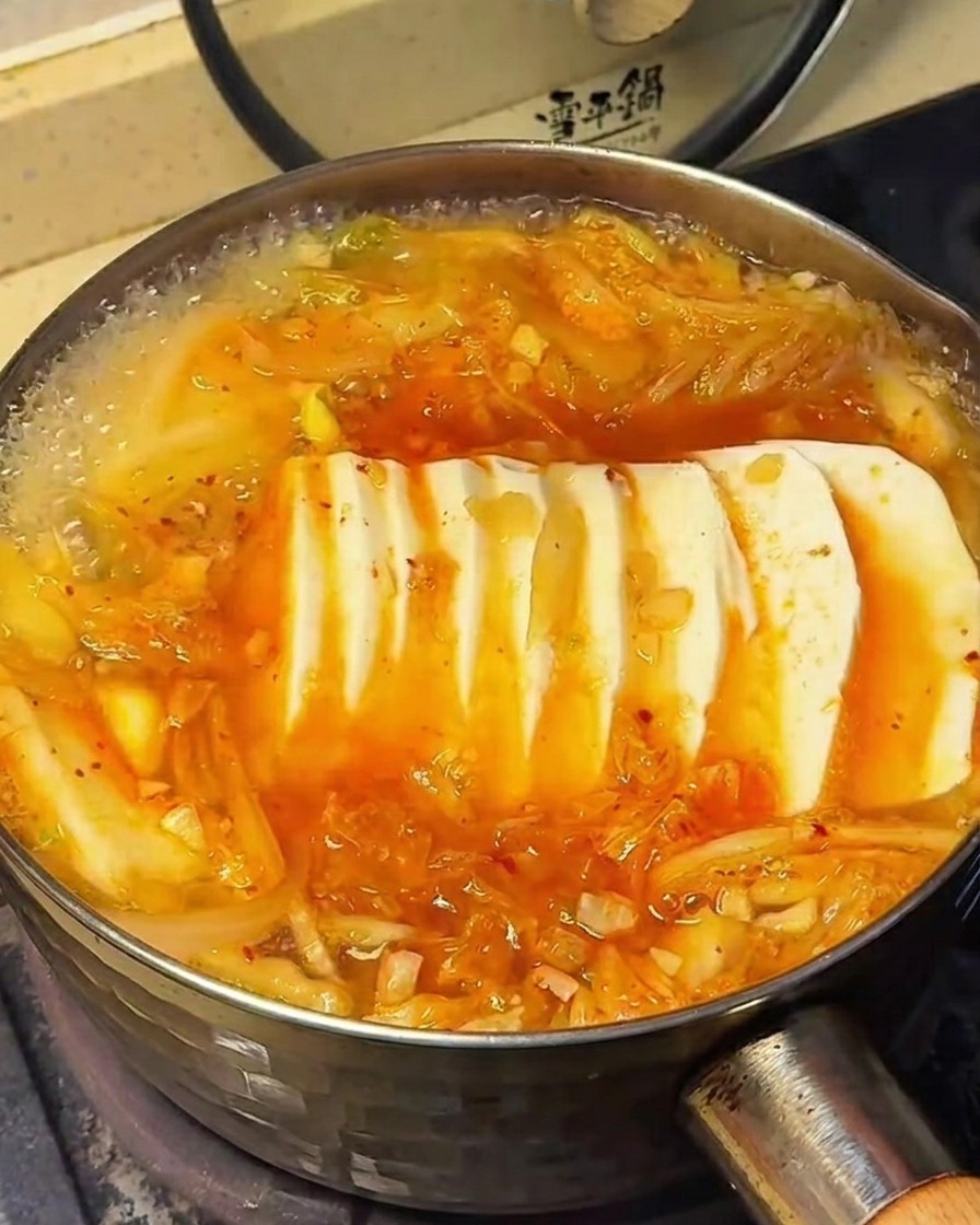 Powierzchnia zupy kimchi z tofu, pokazująca moment posypywania składników przyprawami.