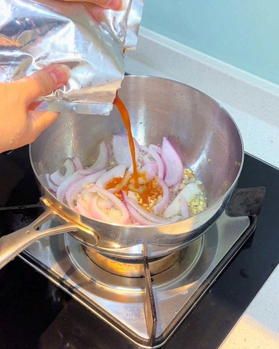 Kimchi wlewane do garnka i mieszane z cebulą i czosnkiem.