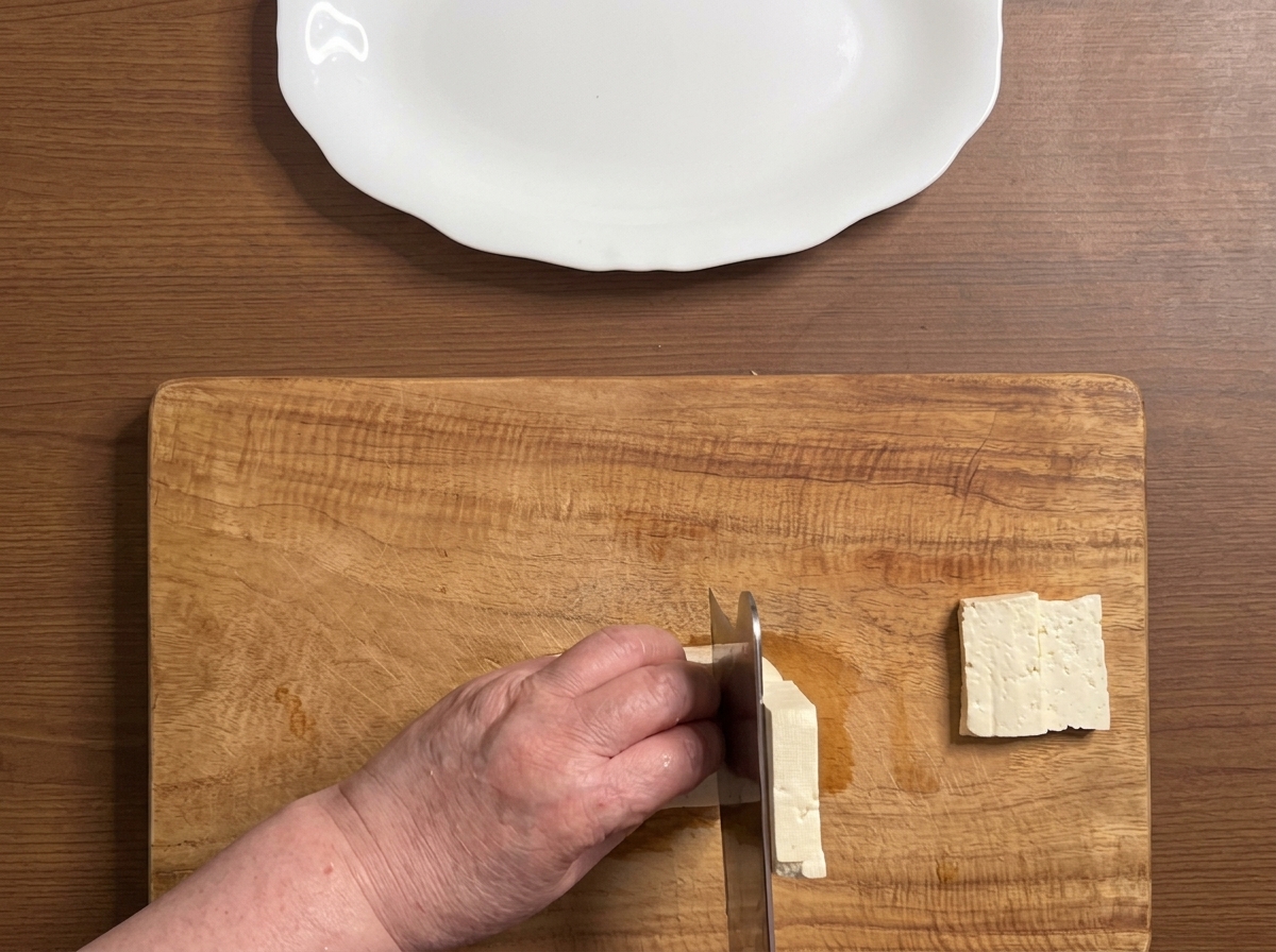 Blok tofu krojony w grube, równe plastry na drewnianej desce.