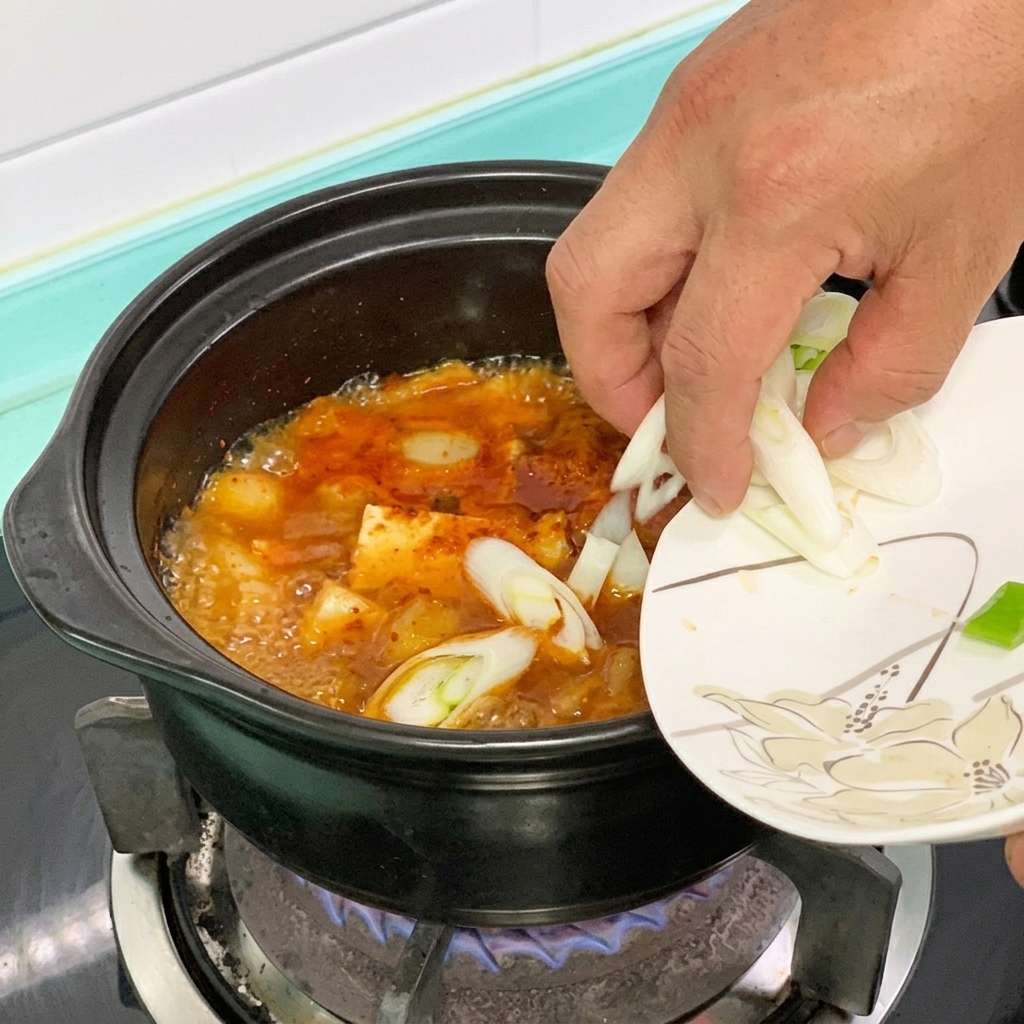 Zielone chili i zielona cebulka wrzucane do garnka z czerwonym gulaszem z tofu.