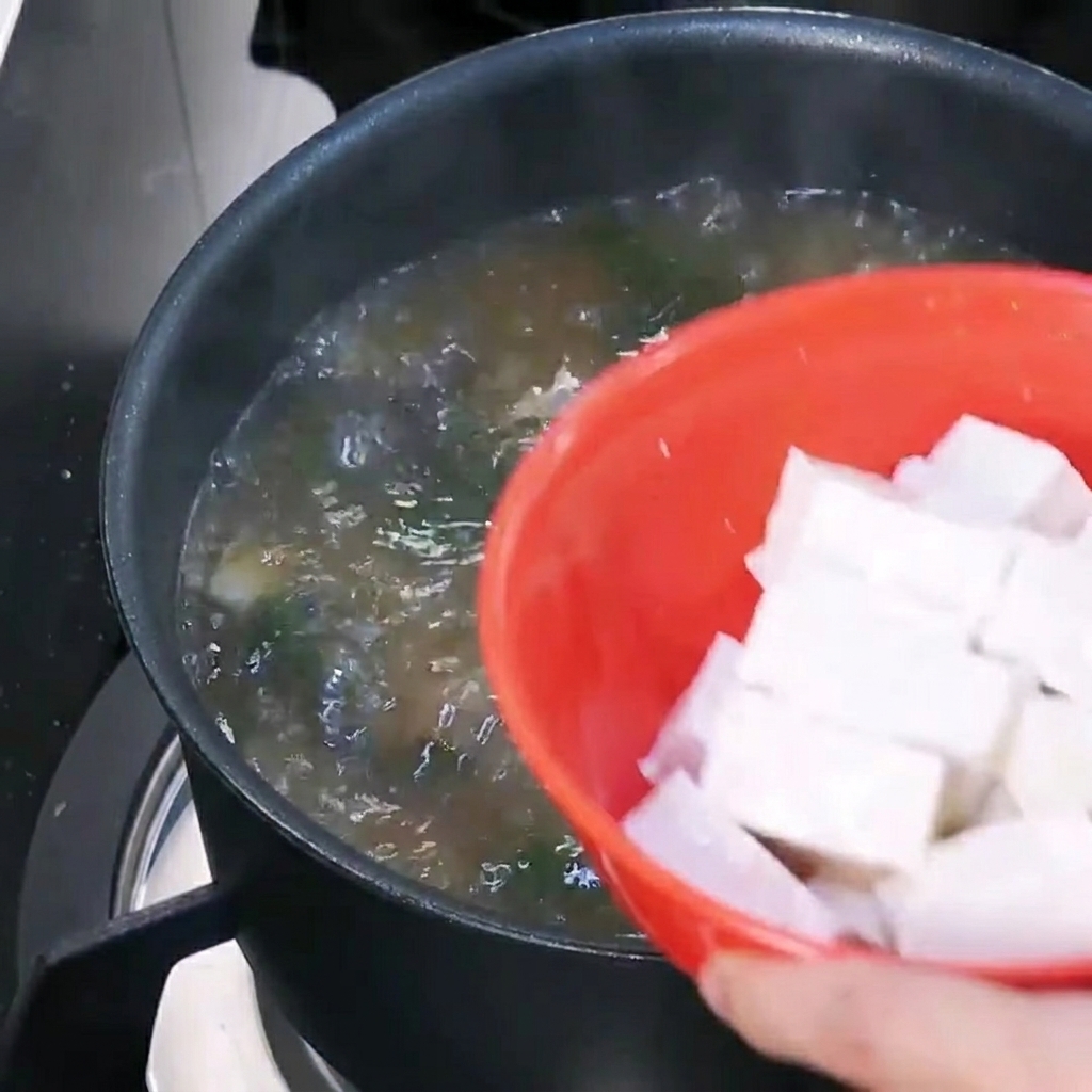 Tofu pokrojone w kostkę dodawane do gotującej się zupy z pasty sojowej.