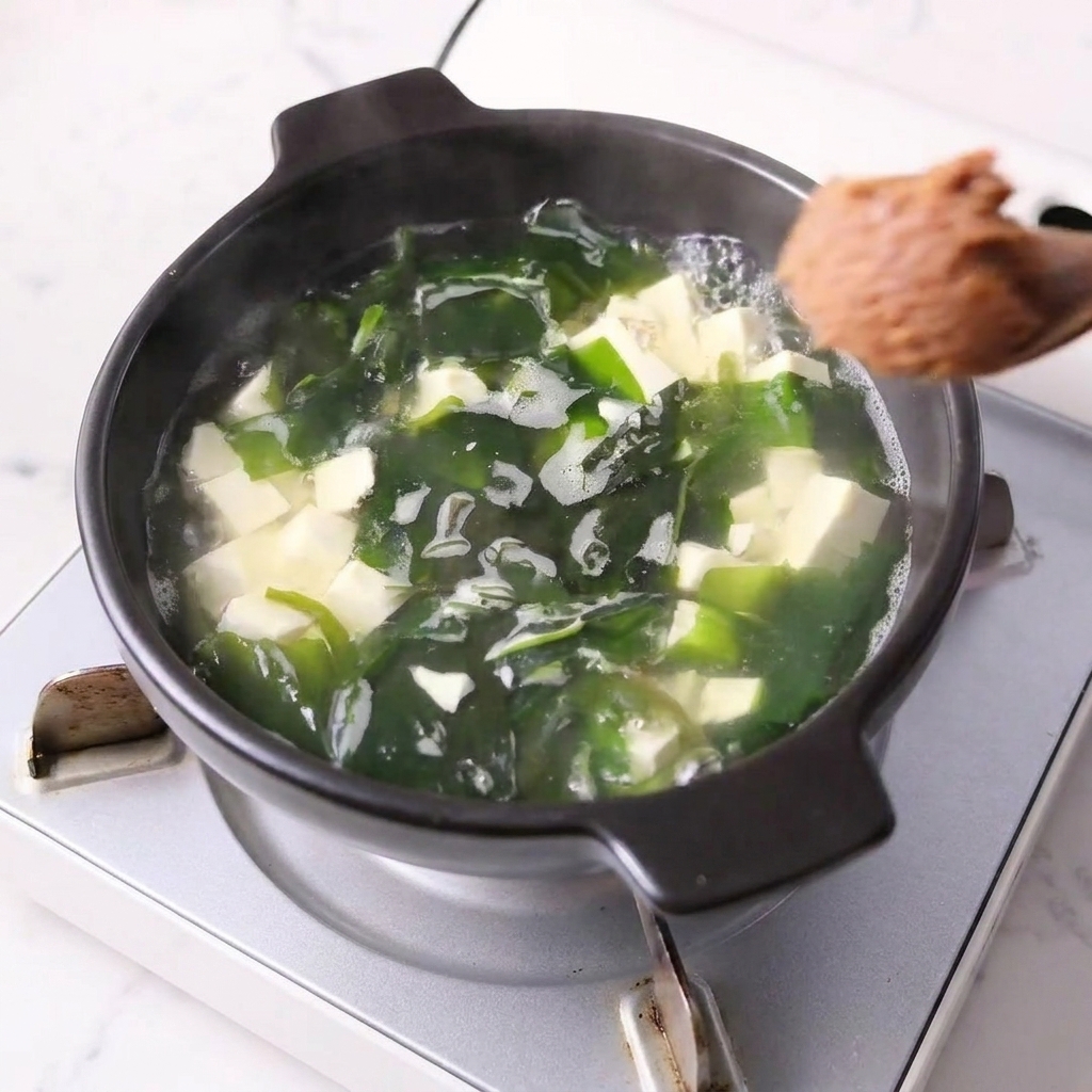Łyżka pasty miso mieszana z wywarem w garnku z tofu i wakame.