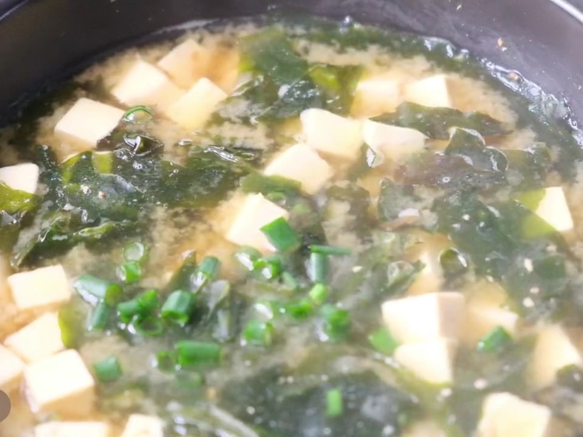 Zbliżenie na garnek z gorącą zupą miso, tofu, glonami i świeżym posiekanym szczypiorkiem.