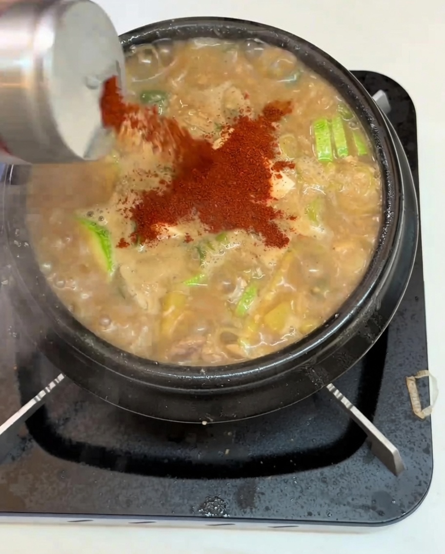 Zbliżenie na czerwoną paprykę chili dodawaną do gulaszu z tofu i warzywami.