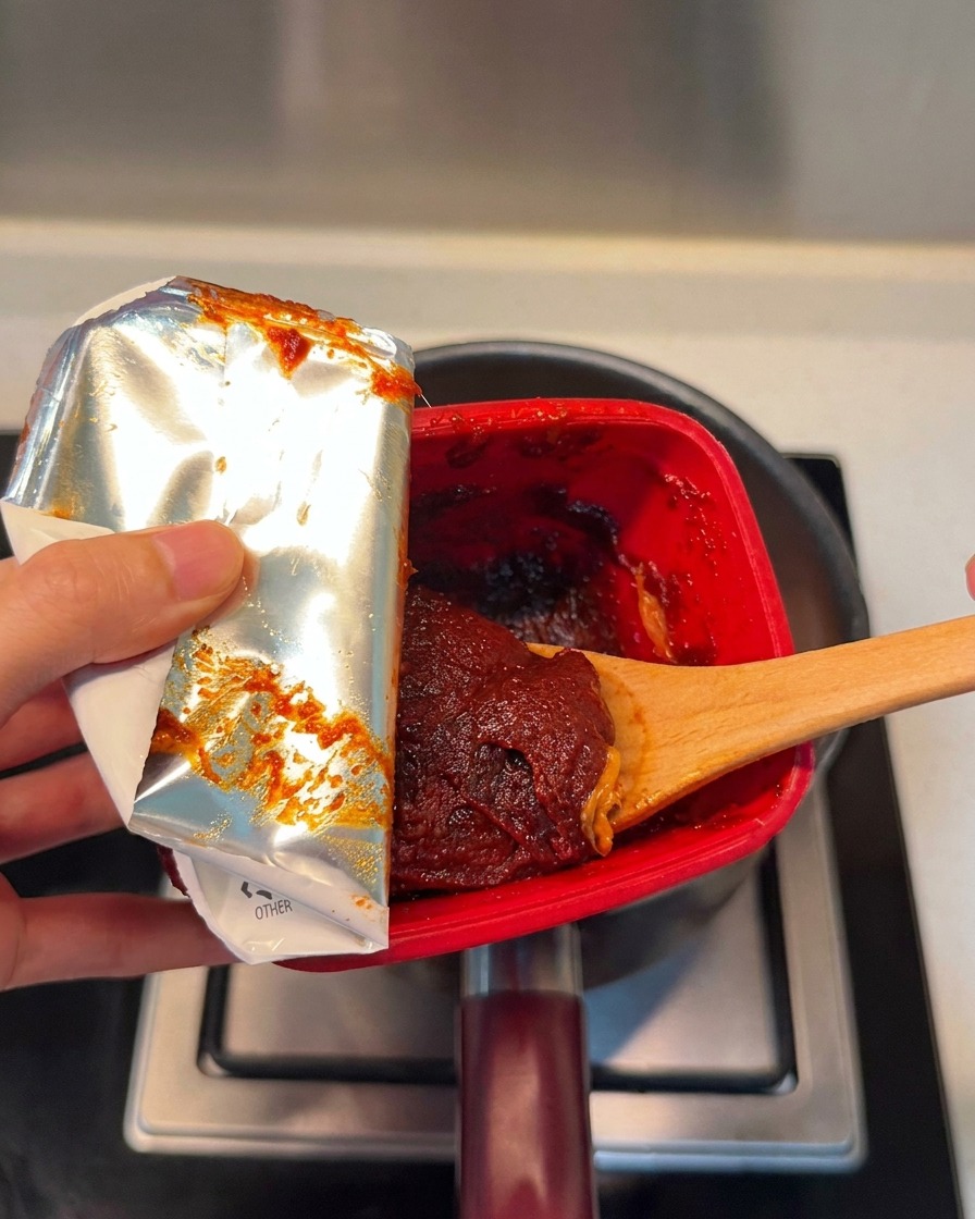 Łyżka bogatej, czerwonej koreańskiej pasty chili dodawana do garnka.