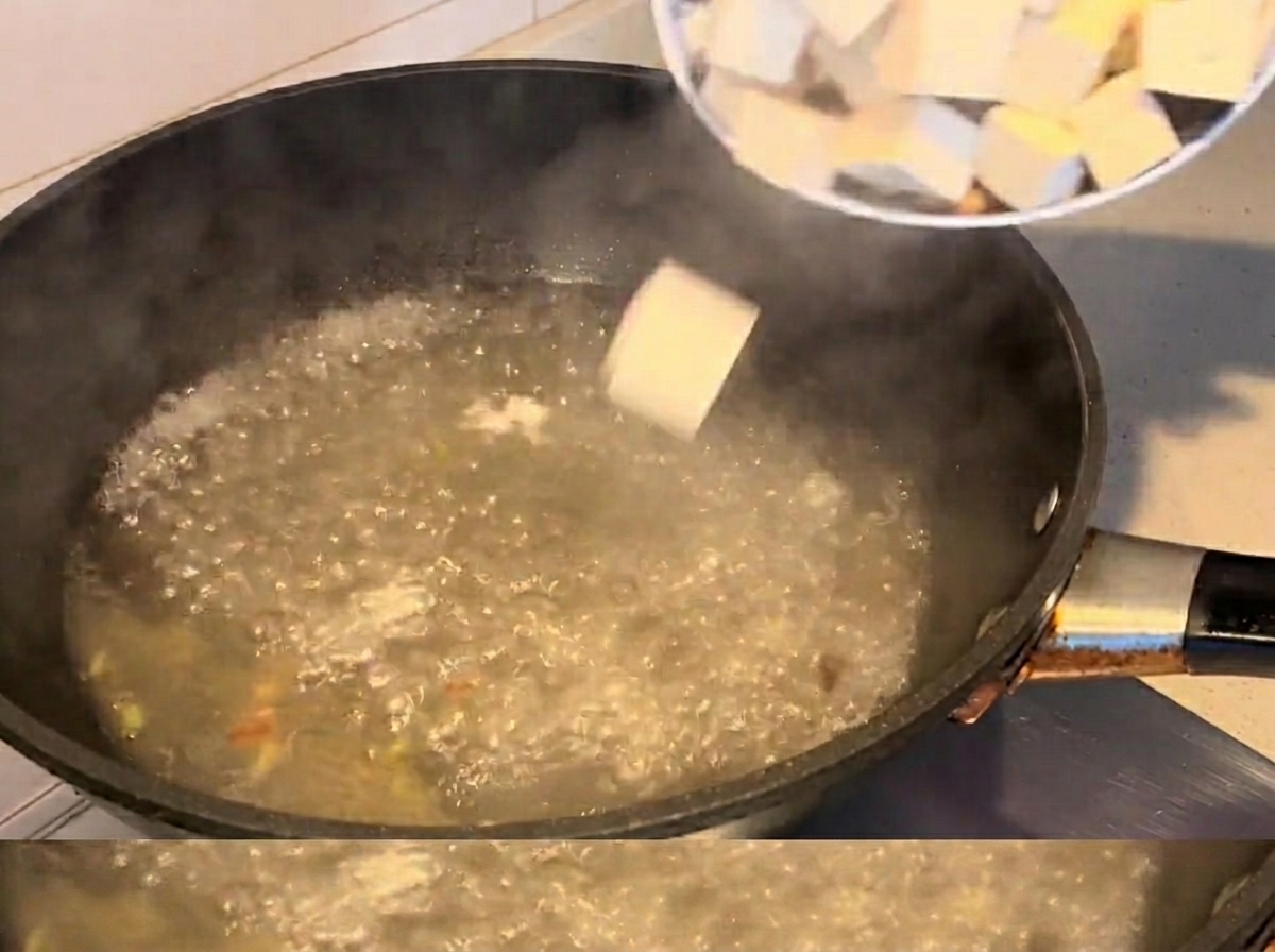 Kostki tofu i małże gotujące się w zupie.