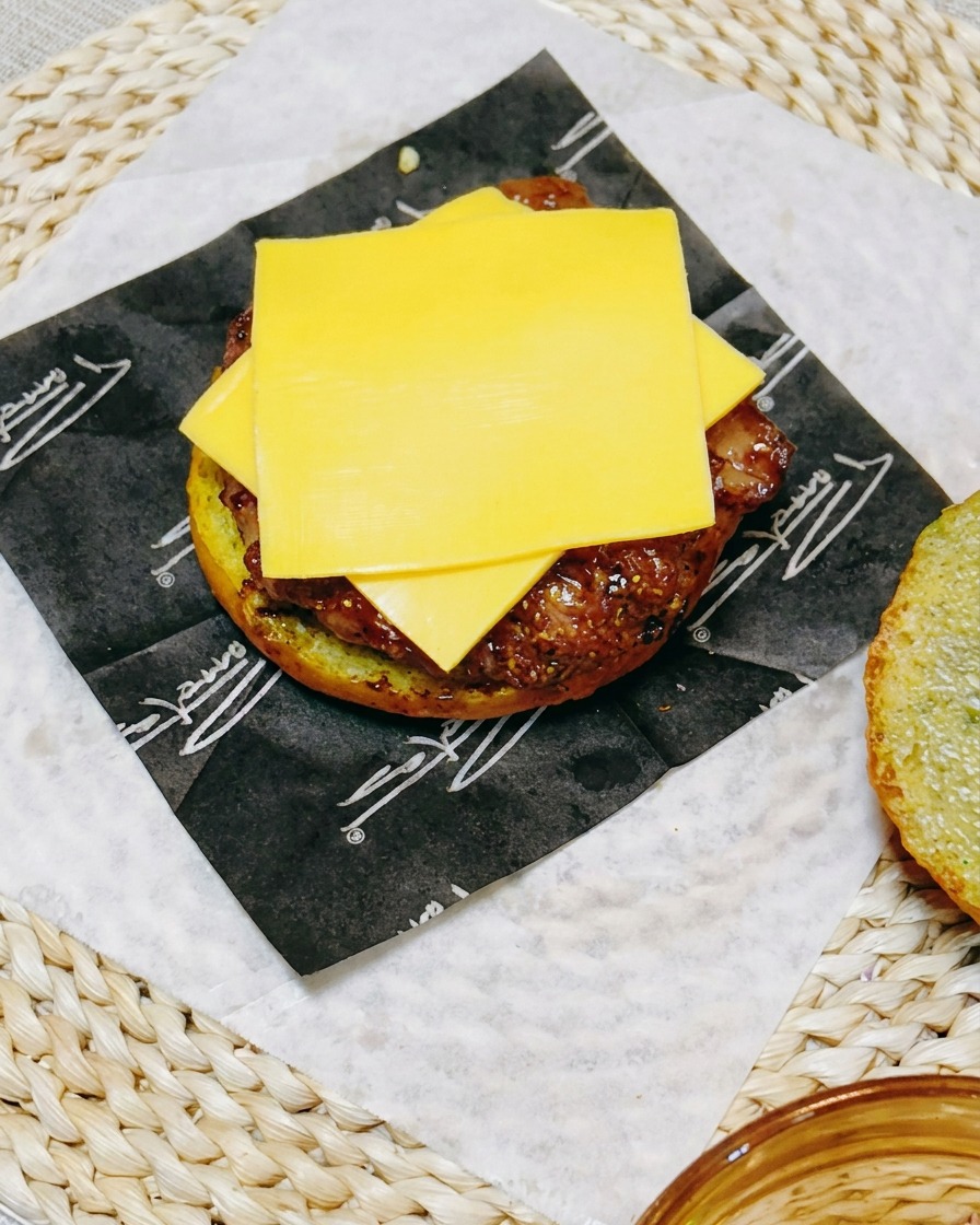 Zbliżenie na składanie burgera pokazujące plaster sera leżący na kotlecie z kurczaka, przykryty świeżymi plastrami ogórka.