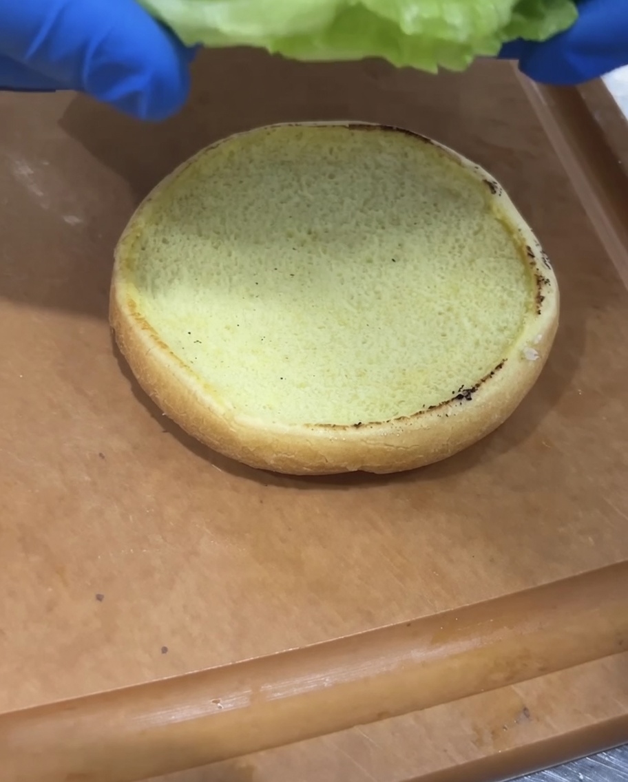 Świeża sałata i plaster pomidora układane na opiekanej bułce do burgera.