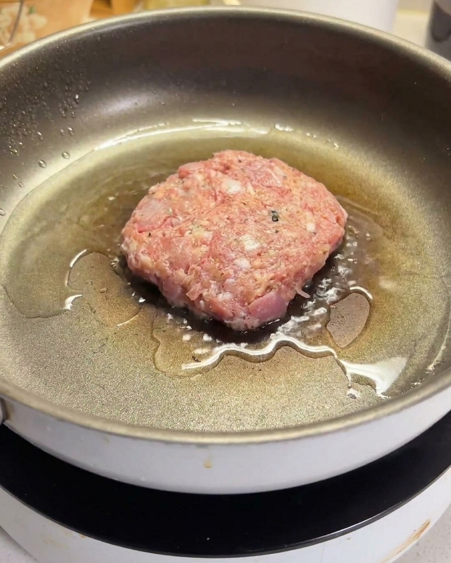 Surowy kotlet wołowy skwierczący na gorącej, naoliwionej patelni nieprzywierającej.