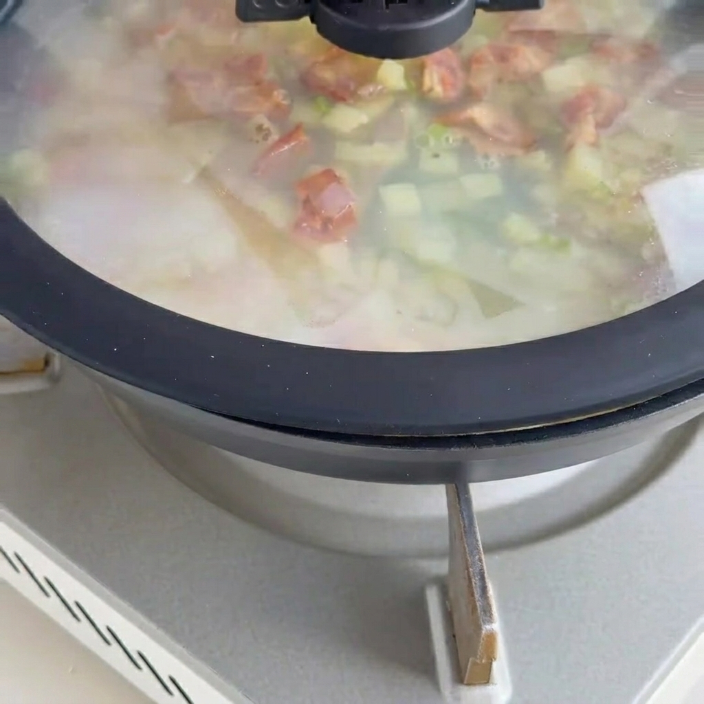Kremowy chowder z małżami gotujący się na patelni z dodatkiem mięsa małży i boczku.
