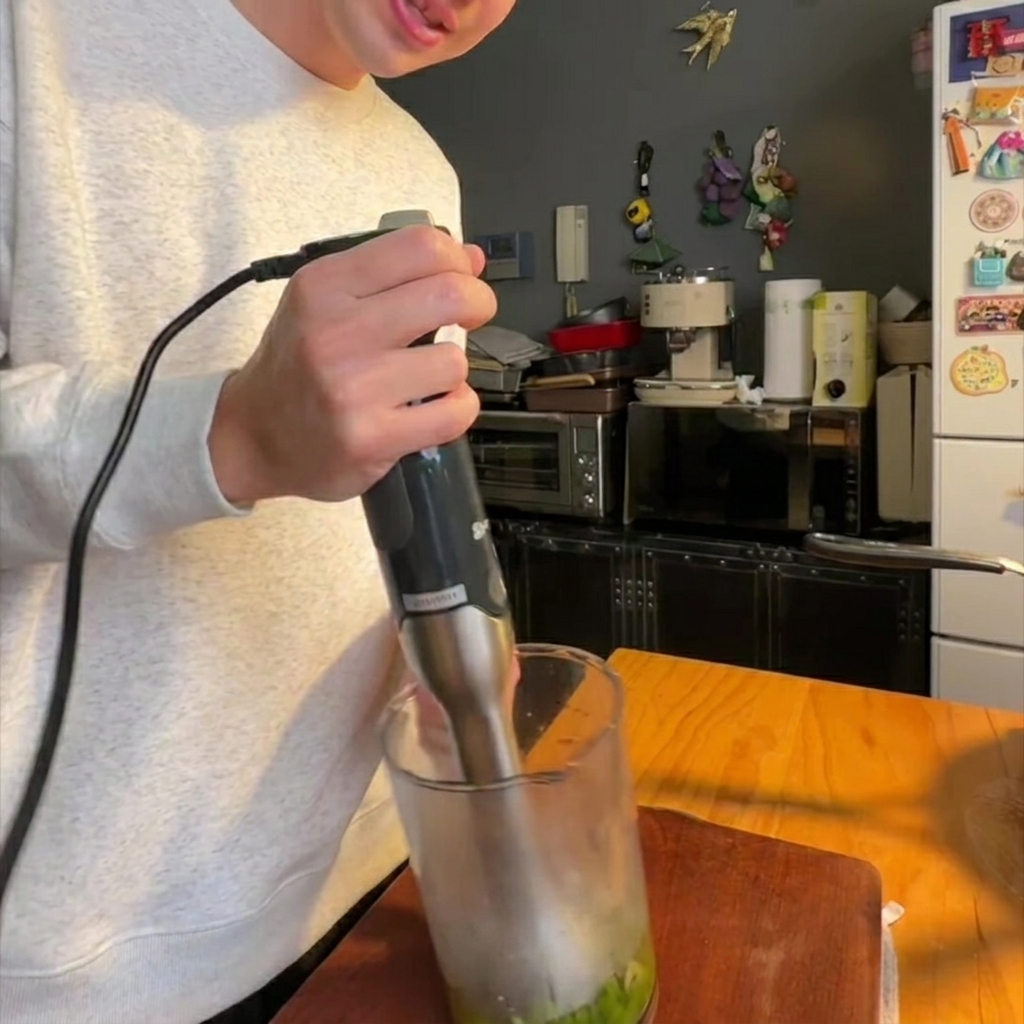 Blender ręczny miksujący ugotowane szparagi z cebulą w szklanym naczyniu na gładką masę.