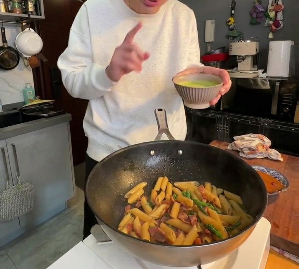 Gładki zielony sos ze szparagów wylewany na makaron penne na patelni i mieszany do połączenia.