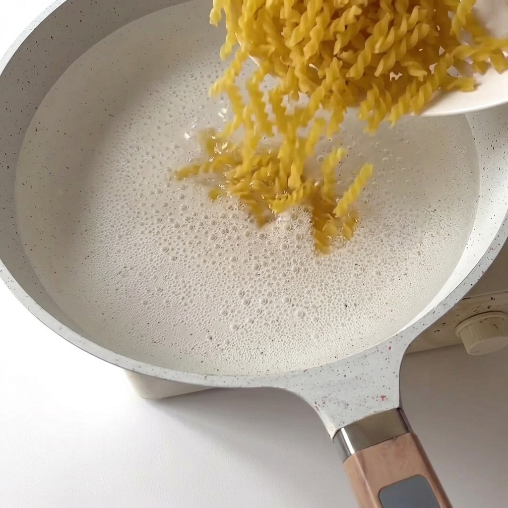 Makaron fusilli wrzucany do garnka z gotującą się wodą.