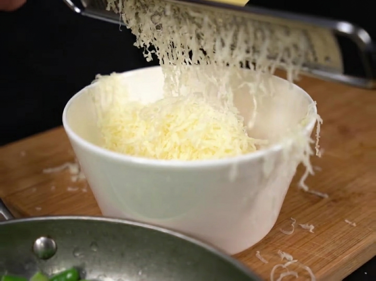 Świeżo starty parmezan wpadający do miski z żółtkami.