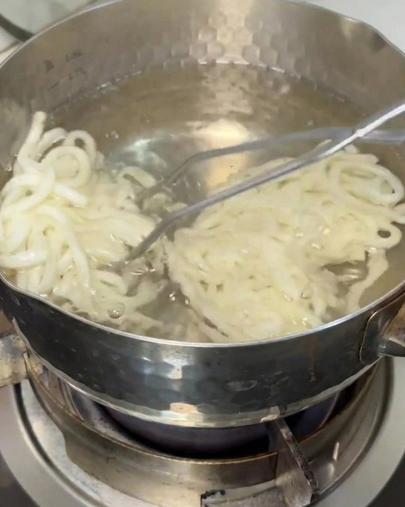 Makaron udon wyciągany z garnka z wrzącą wodą za pomocą kuchennego sitka.
