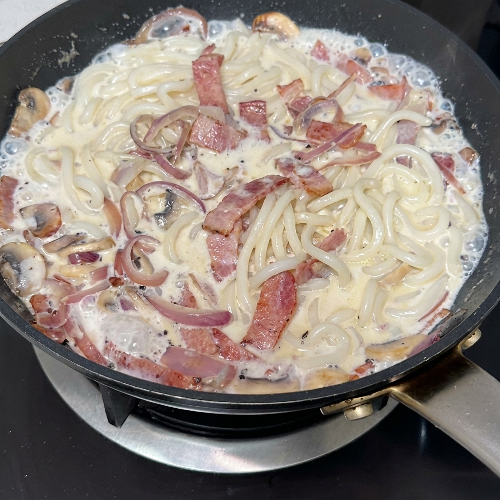 Pasta z czarnej trufli mieszana na patelni pełnej chrupiącego boczku, plasterków grzybów i karmelizowanej cebuli.