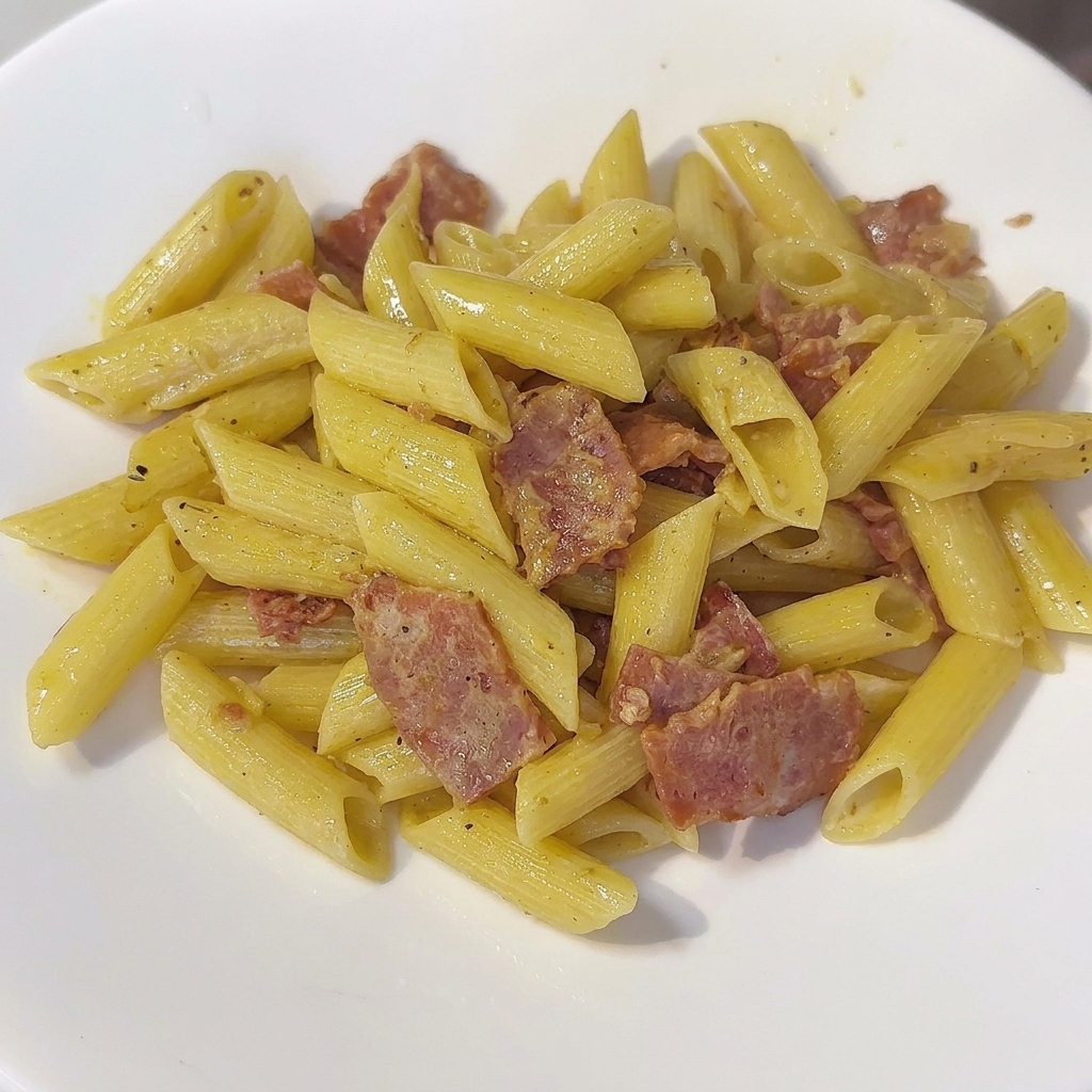 Patelnia kremowego makaronu penne mieszanego szpatułką.