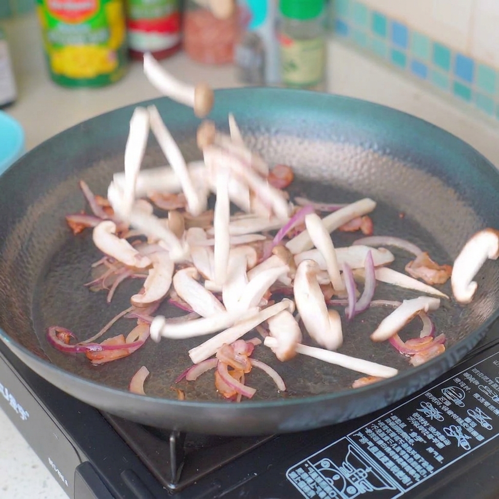 Pokrojone pieczarki i cebula smażone na patelni razem z boczkiem.