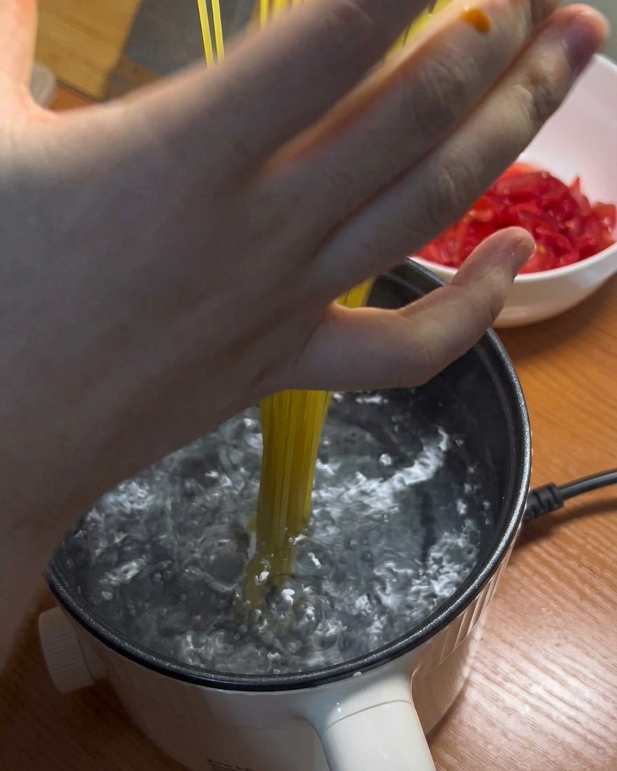 Długie nitki makaronu spaghetti dodawane do garnka z wrzątkiem.