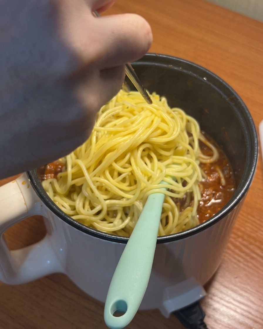 Ugotowane spaghetti dodawane do gotującego się sosu pomidorowo-mięsnego.