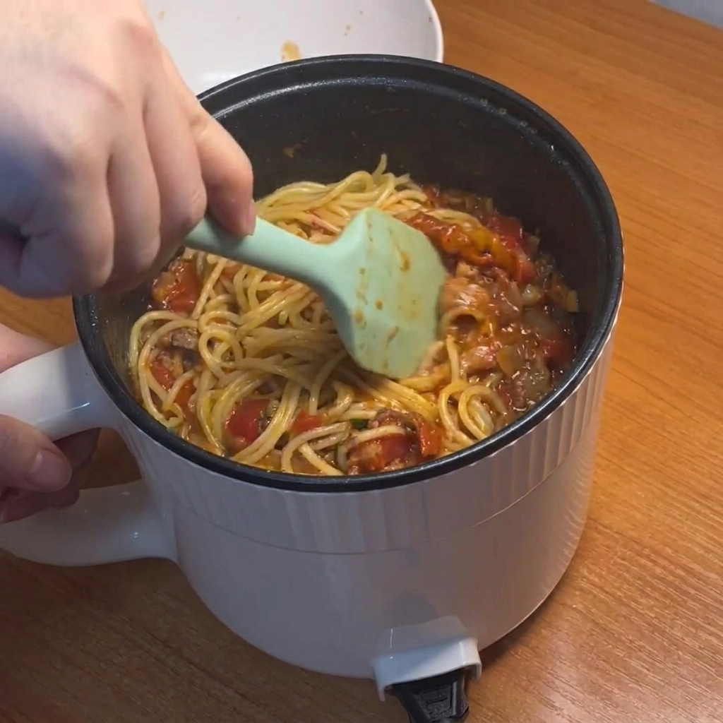 Spaghetti mieszane i pokrywane gęstym, czerwonym sosem z mięsem.