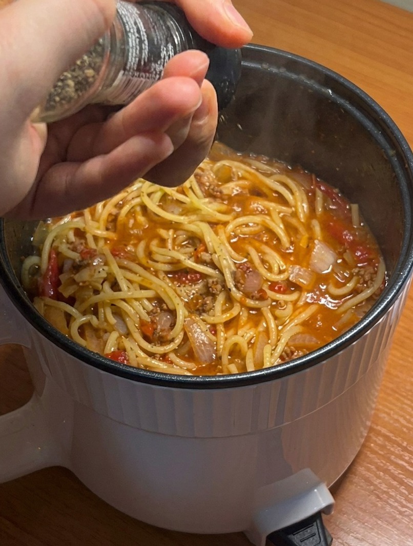Zbliżenie na gotowe spaghetti z sosem mięsnym, doprawiane świeżo tartym czarnym pieprzem.