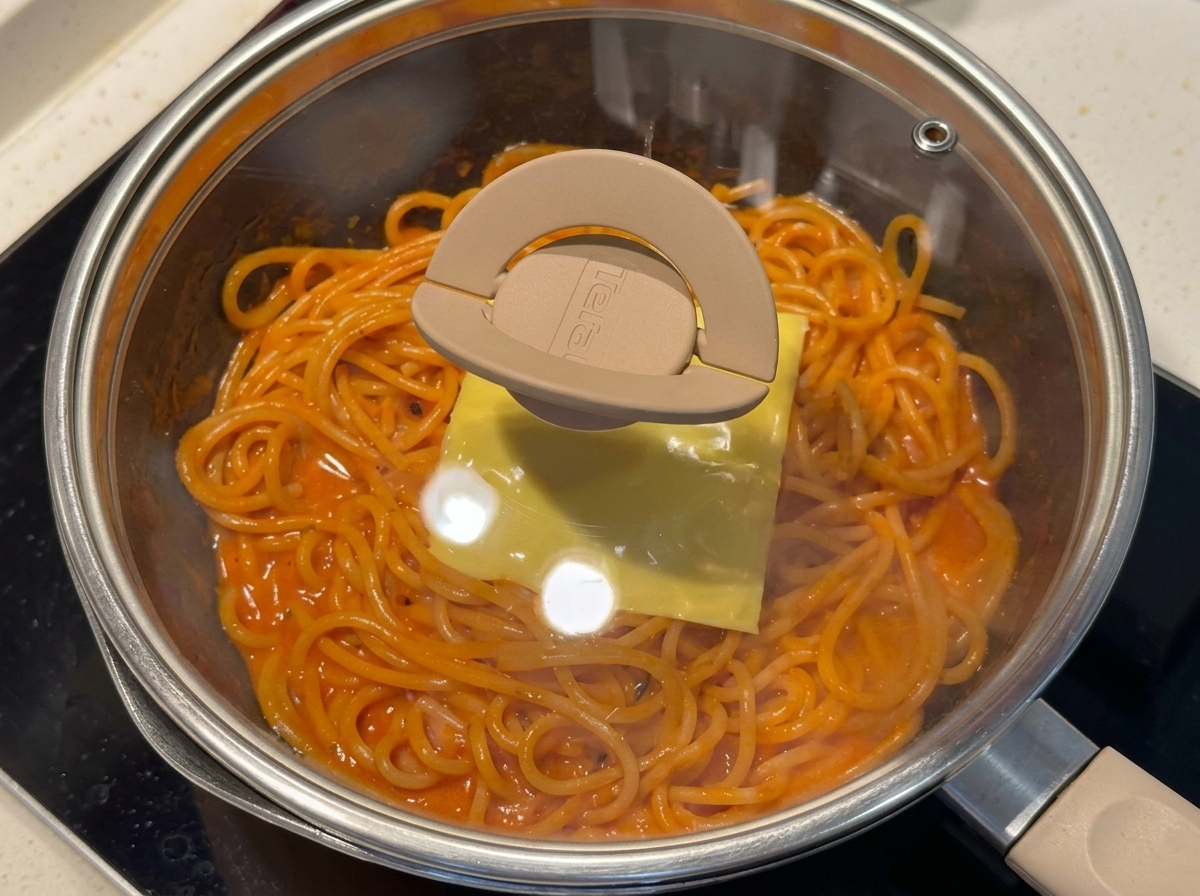 Patelnia ze spaghetti przykryta szklaną pokrywką.