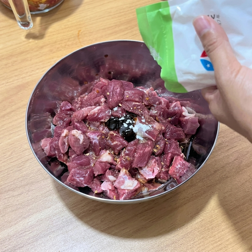 Kawałki wołowiny mieszane z płynnymi przyprawami w metalowej misce.