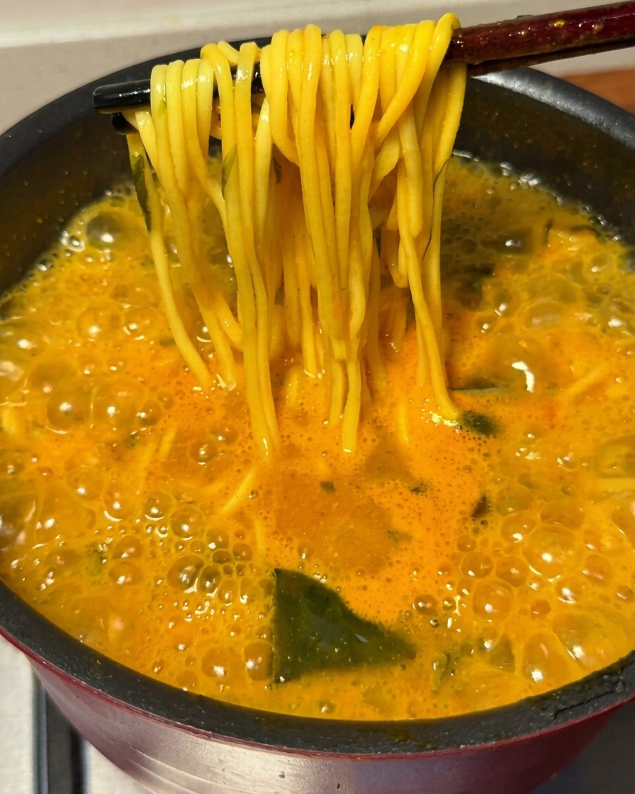 Pałeczki wyciągające wiązkę złotego, ugotowanego makaronu ramen z bulgoczącego, pikantnego bulionu.