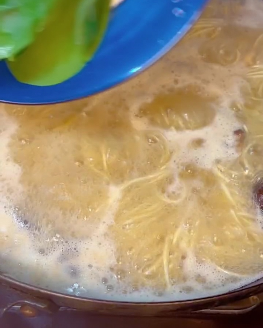 Zielona kapusta bok choy zanurzana w garnku z gotującym się ramenem.