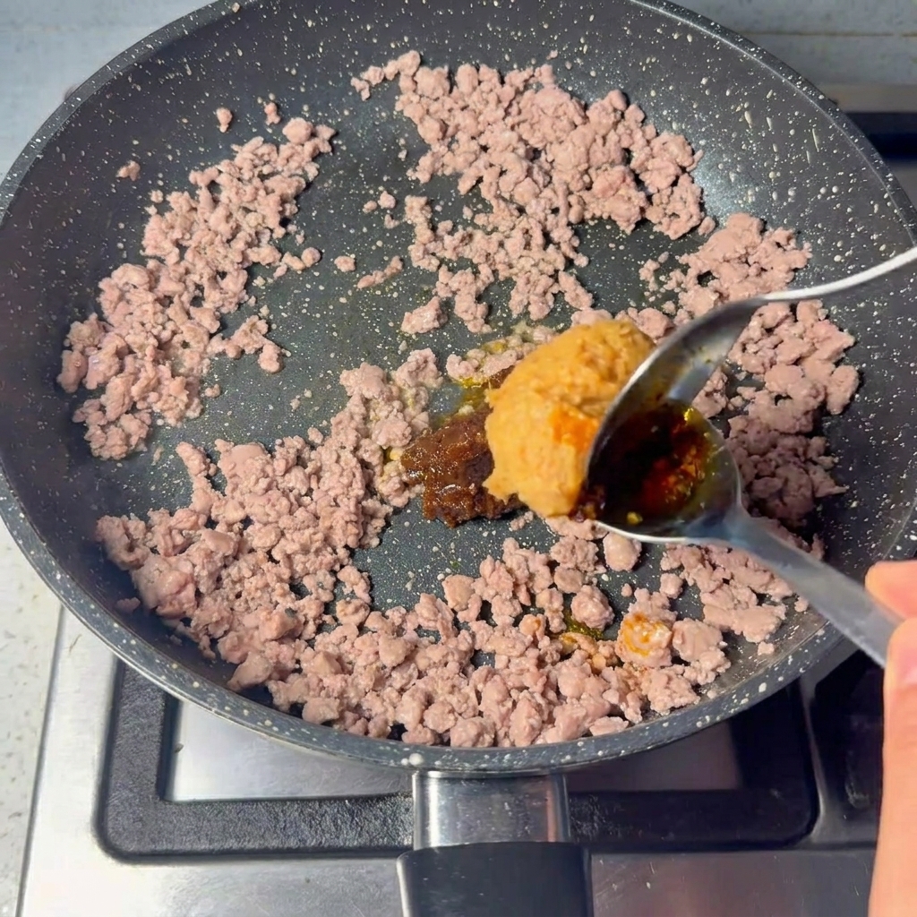 Duża łyżka gęstej, brązowej pasty mieszana z usmażoną mieloną wołowiną.