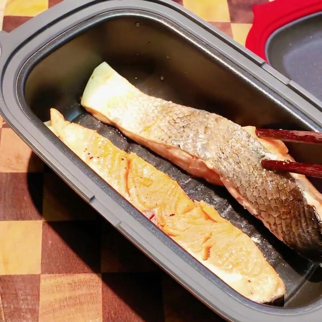 Pałeczki odwracające częściowo ugotowany filet z łososia wewnątrz ciemnej patelni do mikrofalówki.