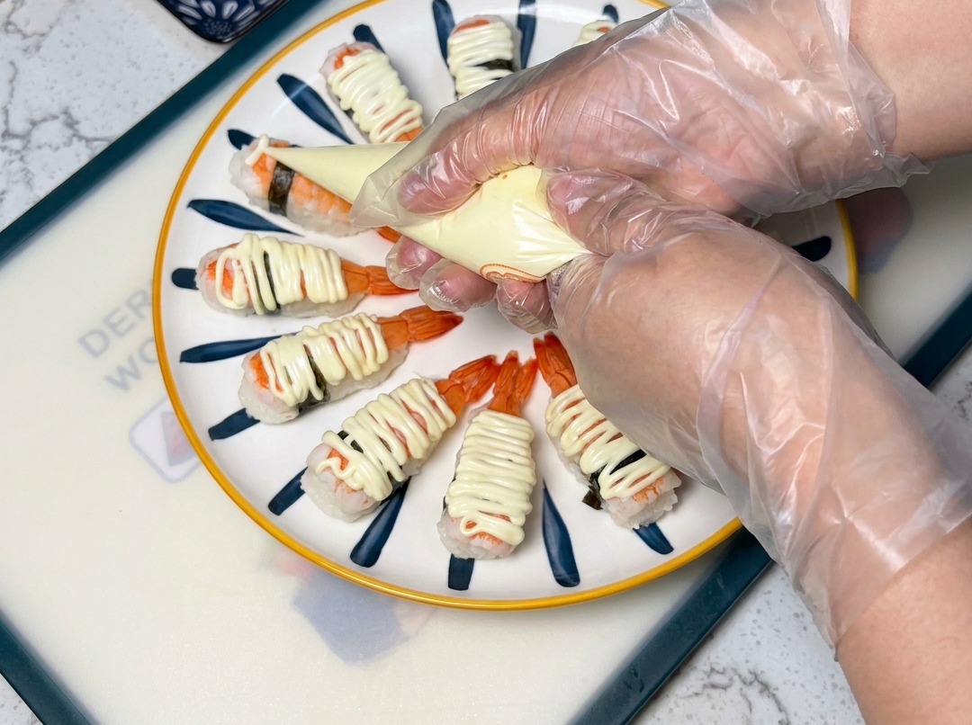 Zbliżenie na rękaw cukierniczy wyciskający majonez na sushi z krewetkami ułożone na talerzu.