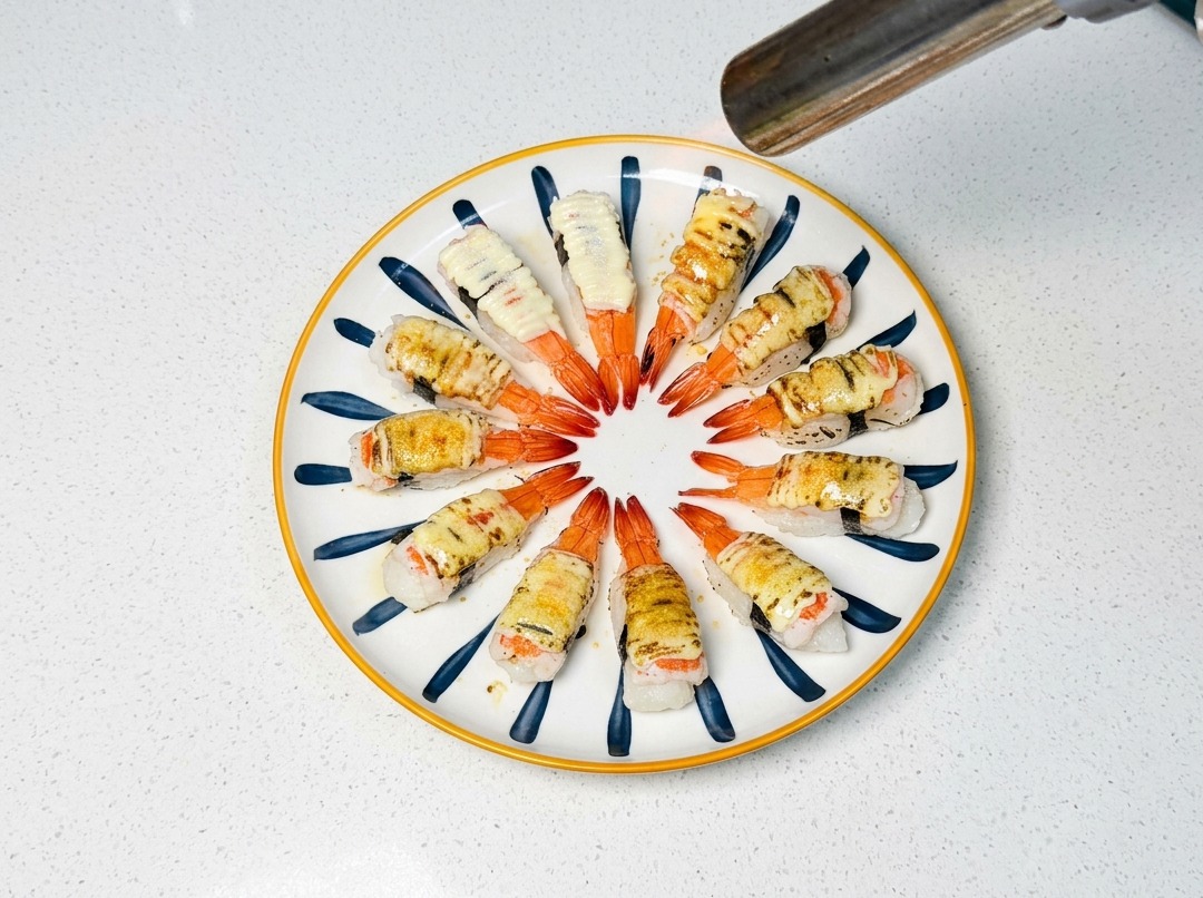 Palnik kuchenny brązowiący warstwę cukru i majonezu na sushi z krewetkami.