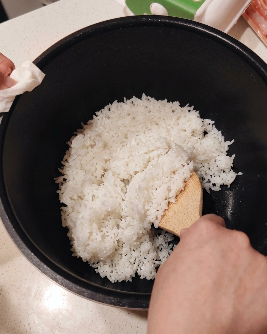 Mieszanie octu do sushi z ugotowanym białym ryżem w misce za pomocą drewnianej łopatki.