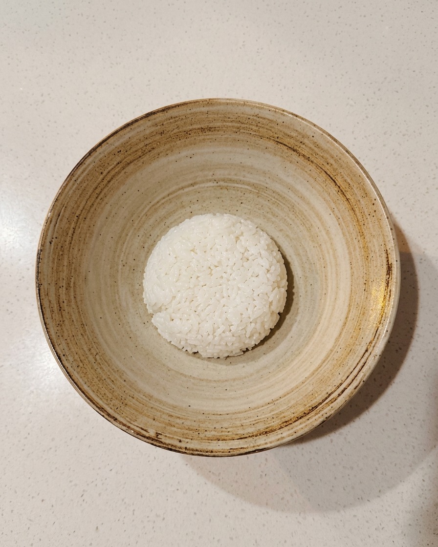 Pojedyncza porcja doprawionego ryżu do sushi umieszczona na środku pustej, rustykalnej ceramicznej miski.