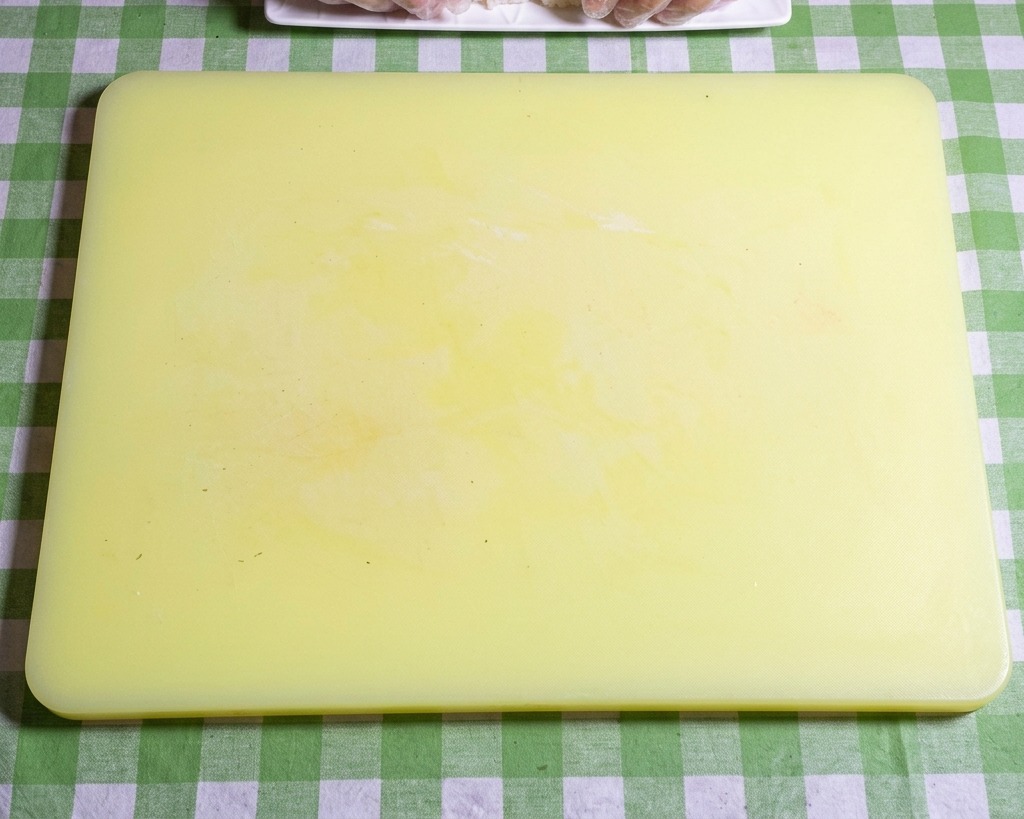 Zbliżenie na dłonie w rękawiczkach formujące lepki ryż do sushi w zgrabne, owalne kulki na żółtej desce do krojenia.