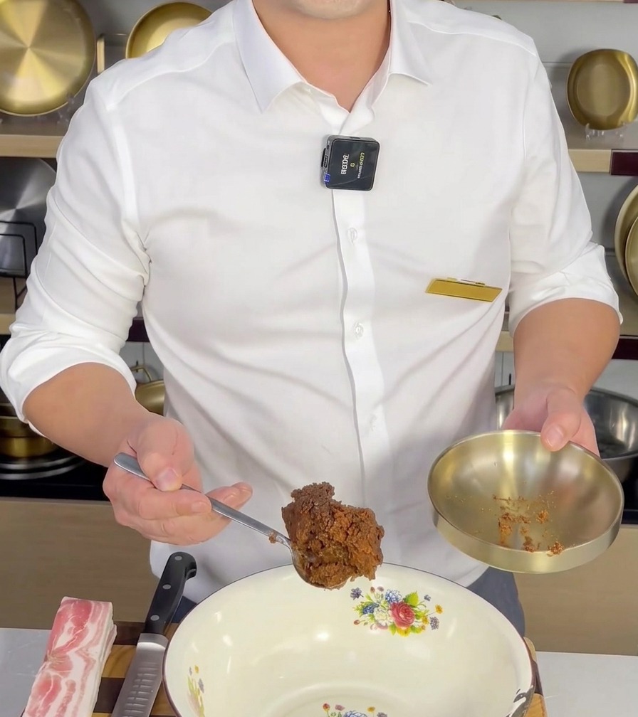 Łyżka pasty Doenjang dodawana do białej miski przed wymieszaniem z innymi składnikami.