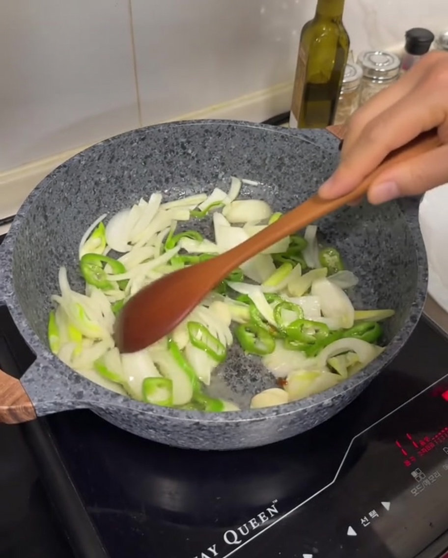 Pokrojona biała cebula, zielone chili i plasterki czosnku smażone na patelni na wytopionym tłuszczu.