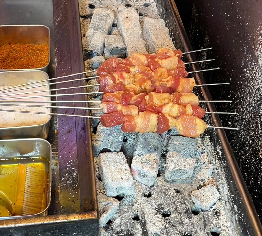 Surowe szaszłyki z boczku ułożone na gorącym grillu węglowym, gotowe do pieczenia.