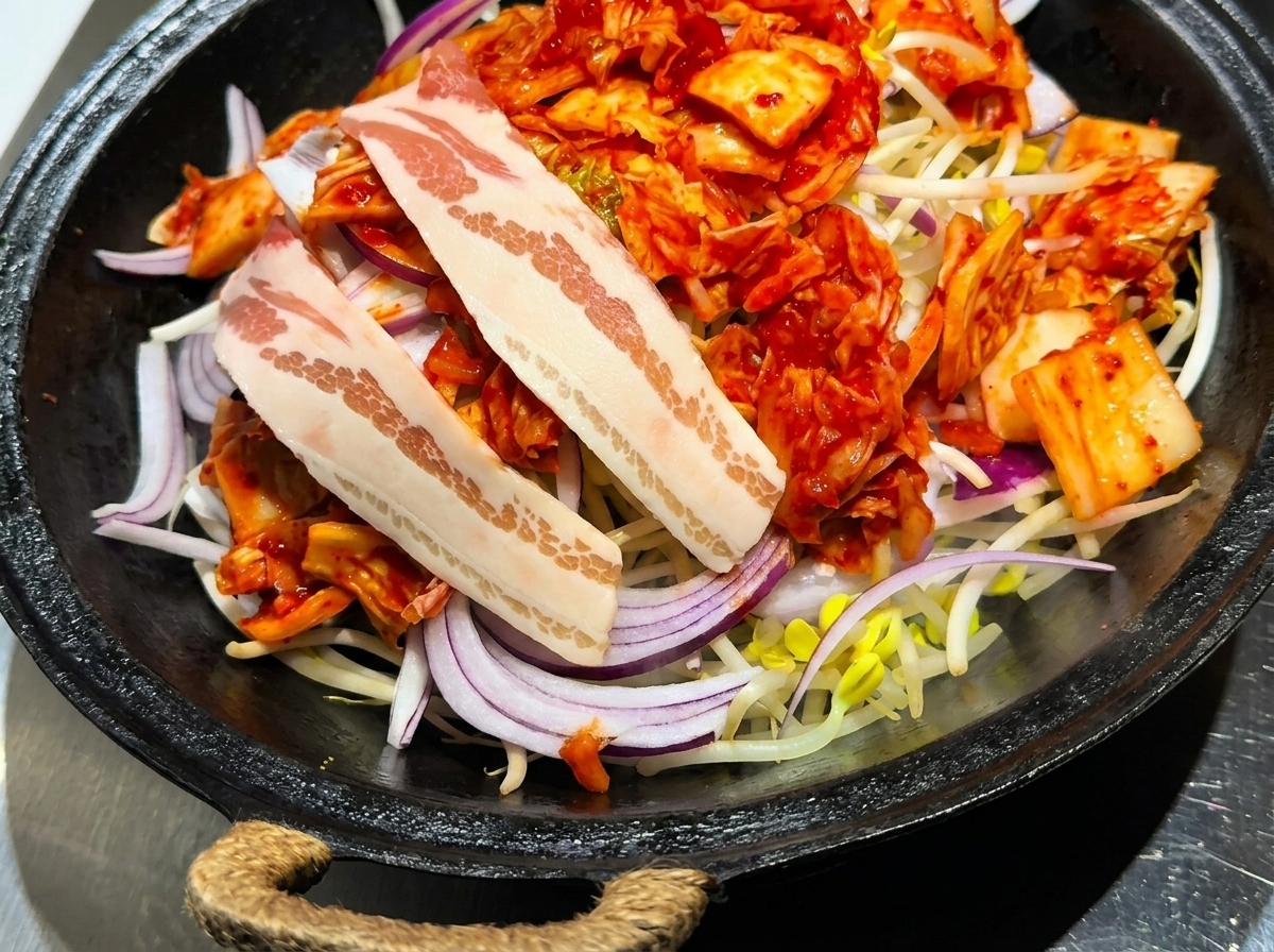 Surowe plastry boczku ułożone starannie na wierzchu warstwy kimchi, cebuli i kiełków.