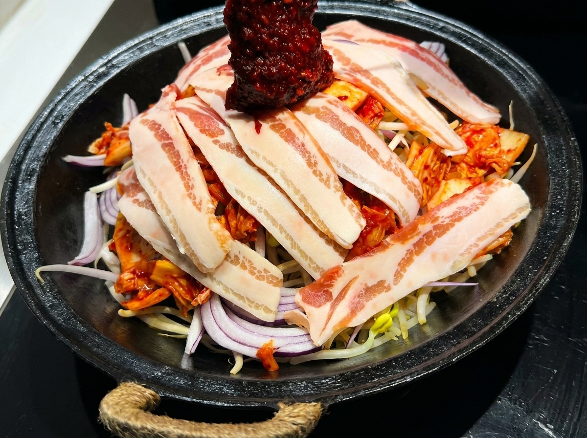 Intensywnie czerwony koreański sos stir-fry rozprowadzany na surowym boczku i warzywach.