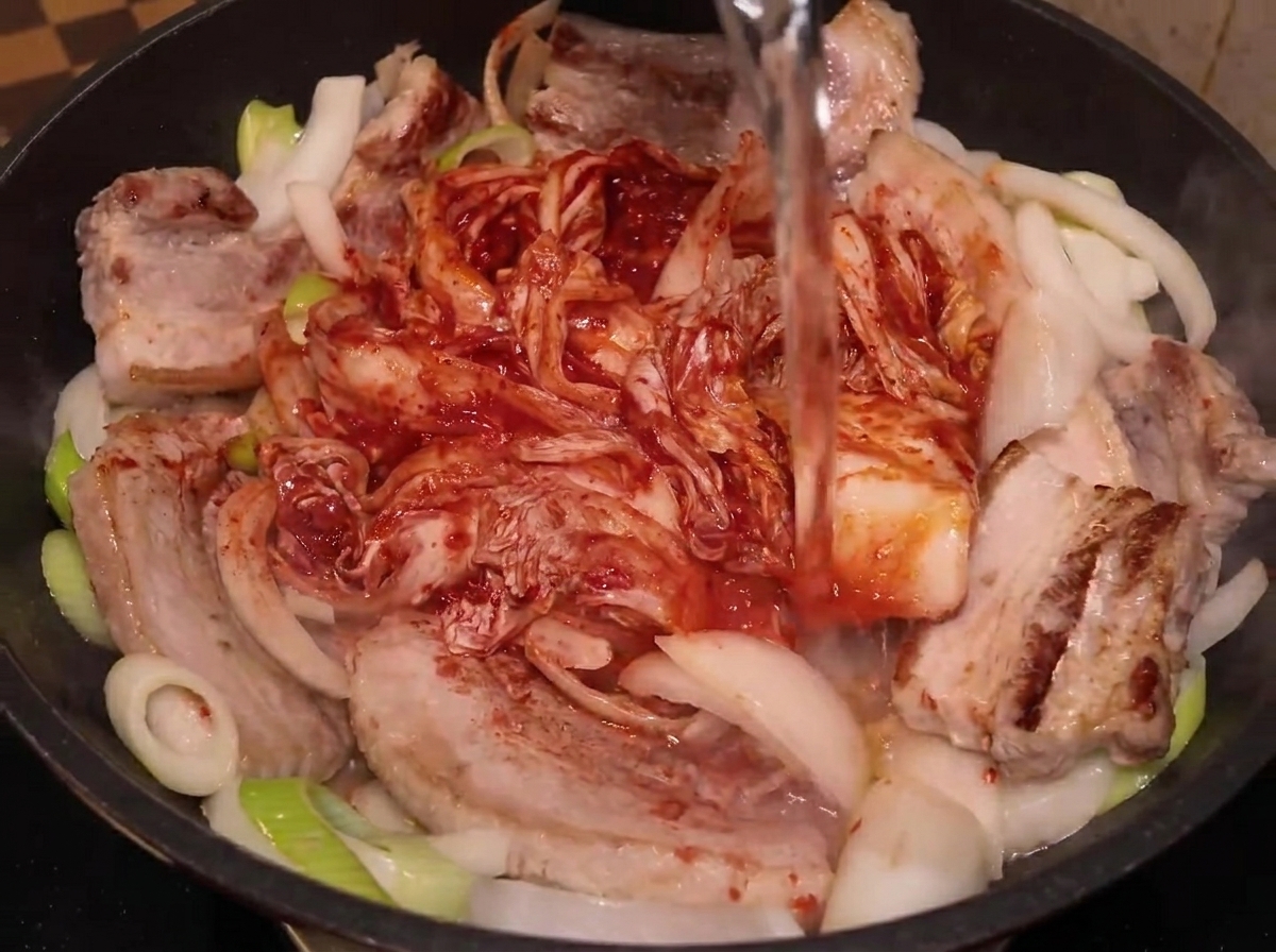 Woda wlewana z butelki do garnka z boczkiem i kimchi.