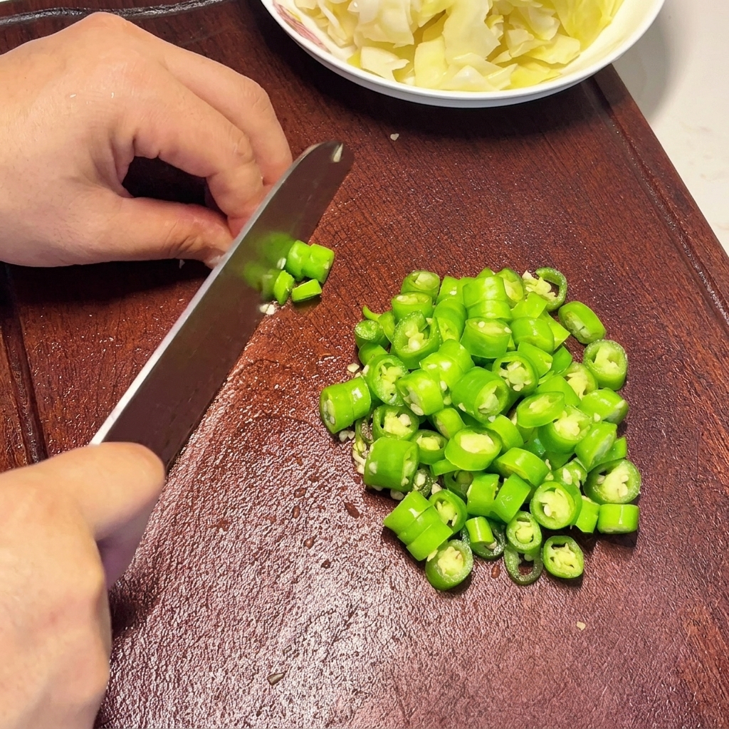 Dłonie siekające żywe zielone chili w równe krążki na ciemnej drewnianej desce.