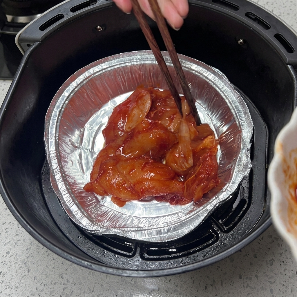 Marynowany kurczak w aluminiowej tacce w koszu frytkownicy.