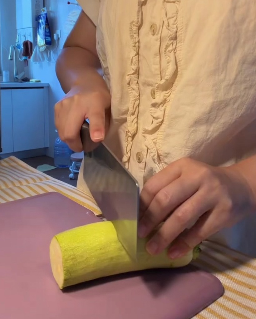 Świeża cukinia krojona w równe półplasterki na fioletowej desce do krojenia.